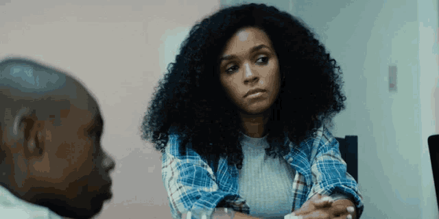 a woman with curly hair is sitting at a table with a man looking at her