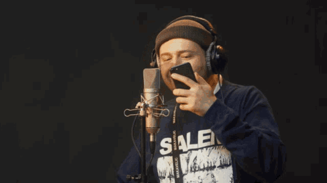 a man wearing headphones and a shirt that says salem is looking at his phone