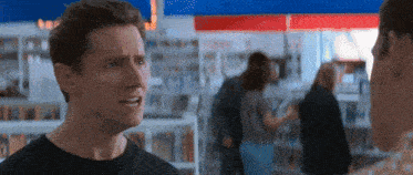 a man is talking to another man in a store while a woman stands in the background .