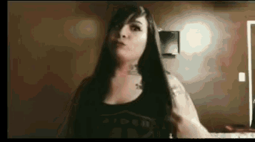 a woman with long hair and a tattoo on her arm is standing in front of a wall .