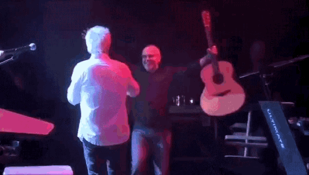 a man holding a guitar on stage with another man
