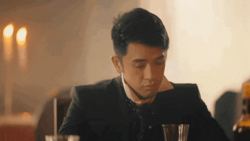 a man in a suit sits at a table with two glasses