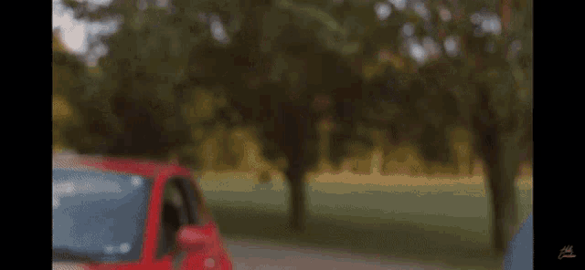 a red car is parked on the side of a road with trees in the background