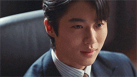 a man in a suit and tie is sitting in a chair and looking at the camera