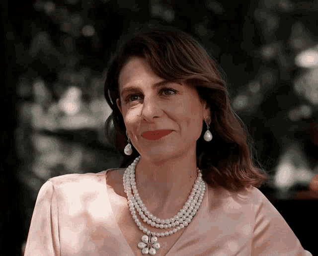 a woman wearing a pearl necklace and earrings looks at the camera