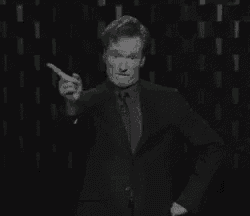 a man in a suit and tie is standing in front of a wall and pointing at his jacket .