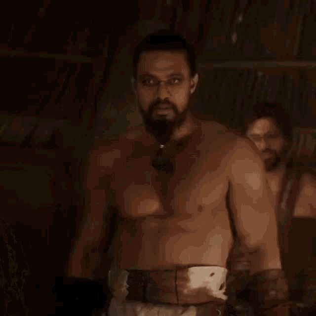 a man with a beard and blue lines on his chest is wearing a belt with the letter g on it