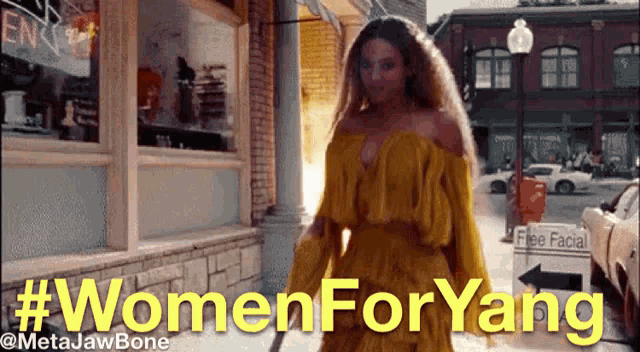 a woman in a yellow dress is walking down a street with #womenforyang written in yellow