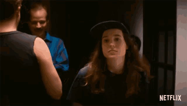 a woman wearing a hat is standing in a dark room with a man standing behind her .