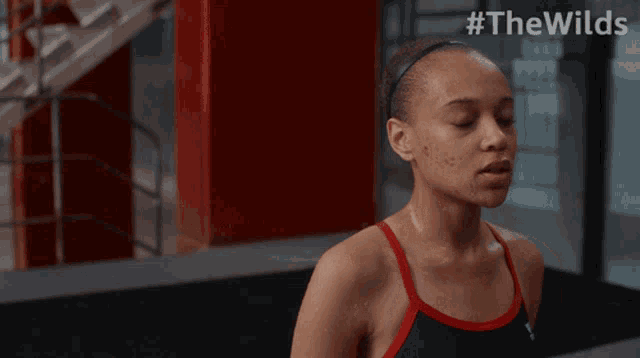 a woman in a black and red tank top is sweating with #thewilds written on the bottom
