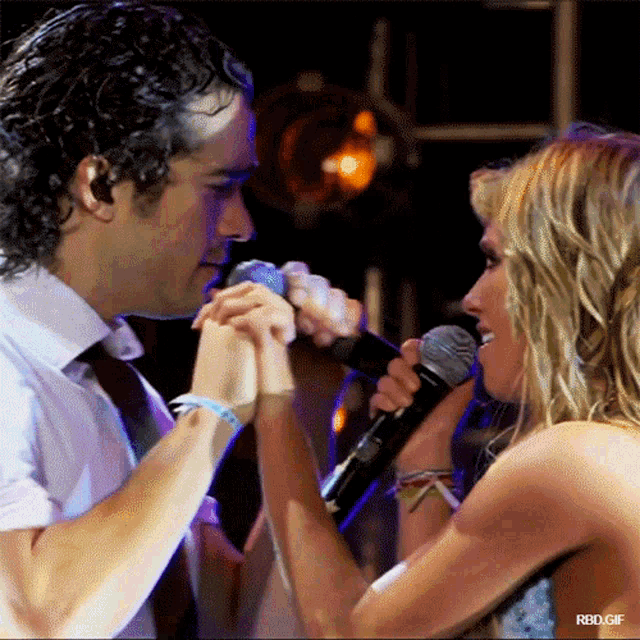 a man and a woman hold hands while singing into microphones with rbd.gif at the bottom