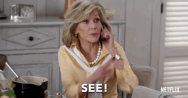 a woman sitting at a table talking on a cell phone and says see