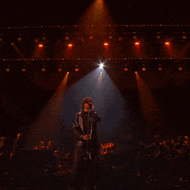 a man singing into a microphone with a large screen behind him