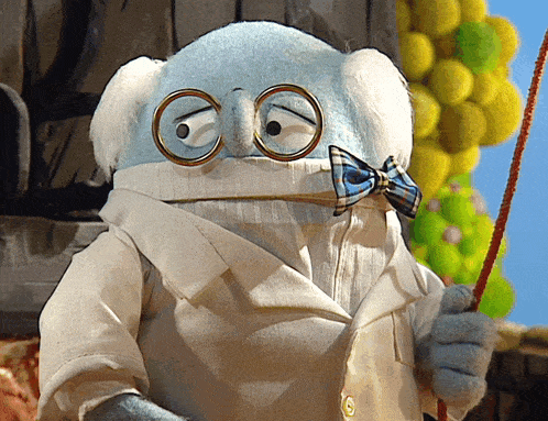 a stuffed animal wearing glasses and a bow tie holds a stick