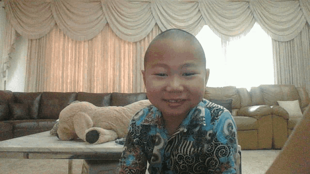a boy with a shaved head sits in front of a couch