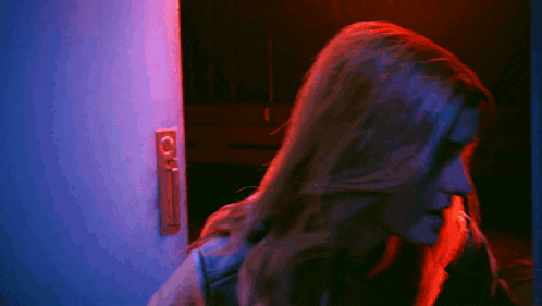 a woman is standing in front of a door with a purple and blue light behind her