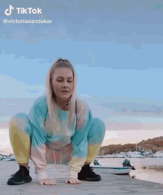 a woman in a tie dye outfit is squatting down on a dock .