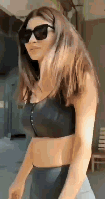 a woman wearing sunglasses and a black crop top is standing in front of a building .