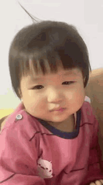a baby girl is sitting on a couch looking at the camera .