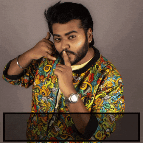 a man wearing a colorful jacket and a watch holds his finger to his lips