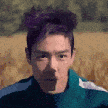 a close up of a man 's face with purple hair and a green jacket .