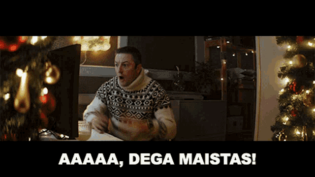 a man in a sweater is standing in front of a christmas tree with the words aaaaa dega maistas written below him