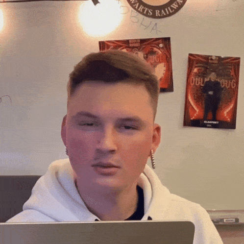 a young man sitting in front of a laptop with a poster on the wall behind him that says oculus