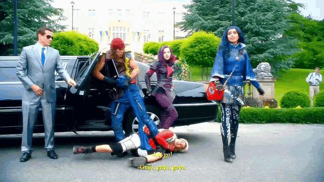 a group of people standing in front of a black limousine with one of them laying on the ground
