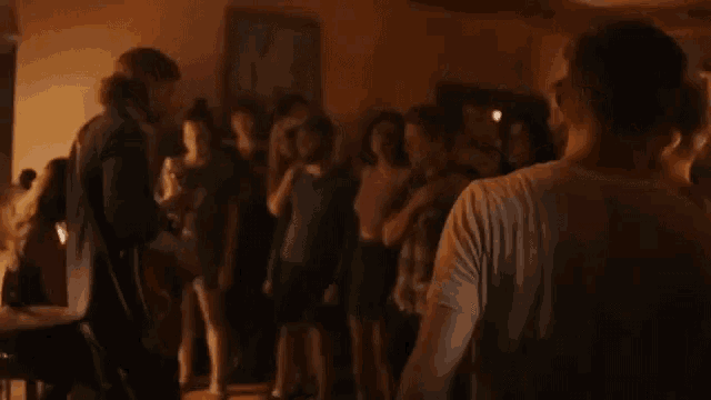 a large group of people are standing in a dark room dancing .