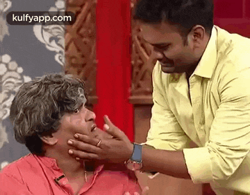 a man in a yellow shirt is touching the face of another man .