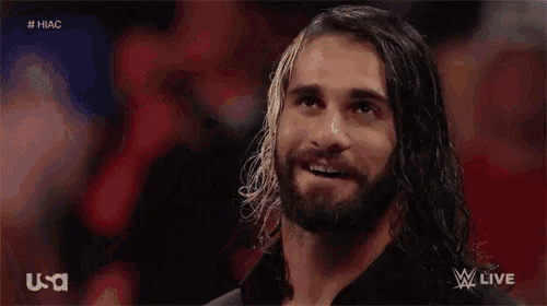 a man with long hair and a beard is smiling during a wrestling match on tv .