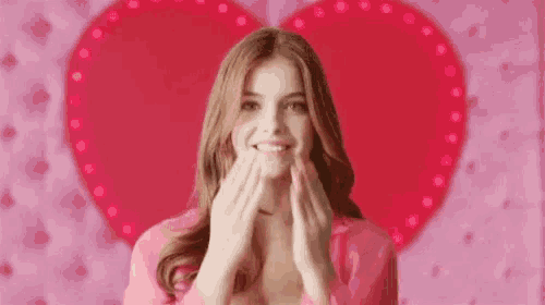 a woman is making a heart shape with her hands in front of a pink heart .