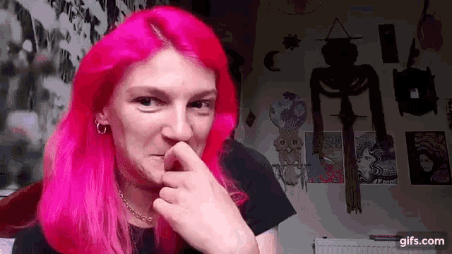 a woman with pink hair is holding her nose .