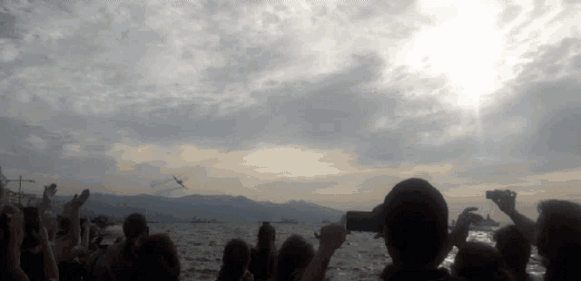 a group of people are taking pictures of a plane flying over the water