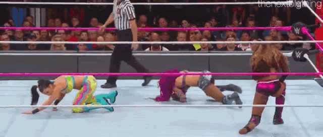 a group of women are wrestling in a ring with a referee in the background .