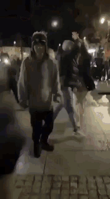 a group of people are walking down a sidewalk at night holding hands .