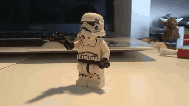 a lego storm trooper is holding a gun on a table in front of a laptop