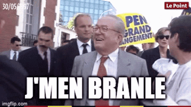 a man in a suit and tie laughs while holding a sign that says " pen grand rangement "