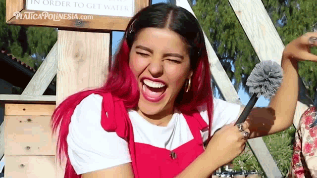 a woman with red hair is laughing and holding a brush in front of a sign that says in order to get water