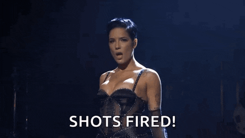 a woman in a black bra and gloves is standing on a stage and says `` shots fired ! ''