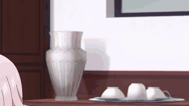 a vase sits on a table next to a tray of cups and saucers