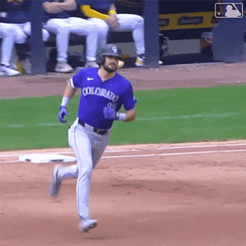 a baseball player wearing a purple colorado jersey is running to first base .