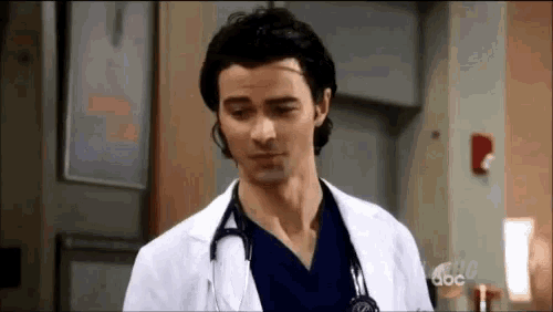 a man in a white lab coat with a stethoscope around his neck is standing in a room .