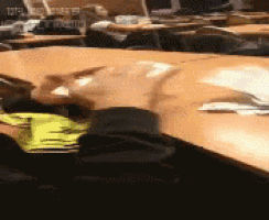 a blurred image of a classroom with a person sitting at a desk with a yellow shirt on