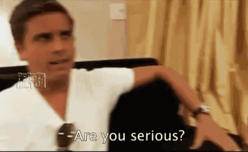 a man in a white shirt is sitting on a couch and asking are you serious .