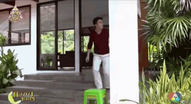 a man in a red shirt is standing in front of a house with a green stool on the ground