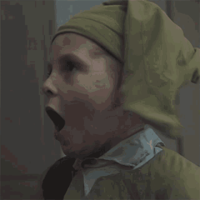 a young boy wearing a green hat and a white shirt is making a surprised face
