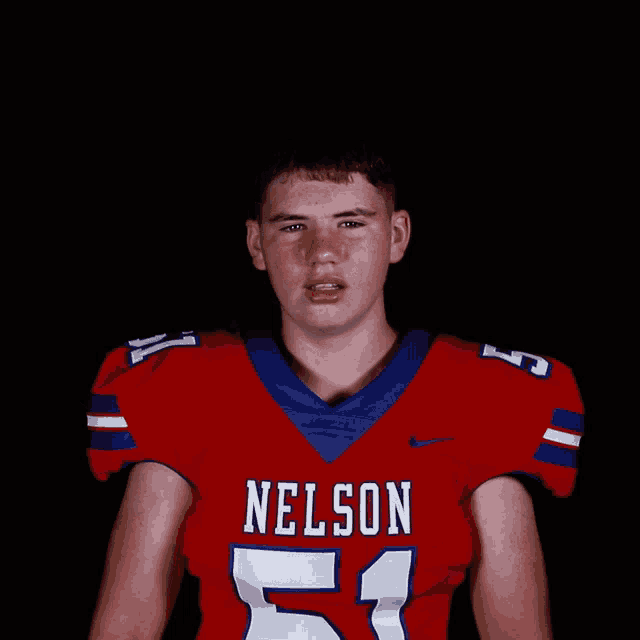 a young man wearing a nelson 51 jersey stands with his arms in the air