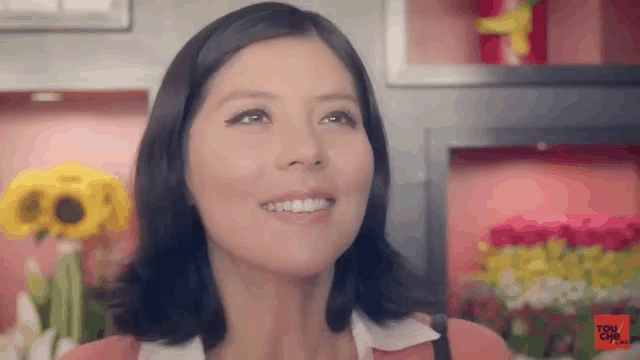 a woman is smiling in front of a display of flowers and looking up .
