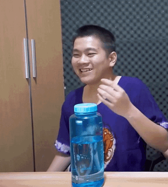 a man in a purple shirt is smiling next to a blue bottle